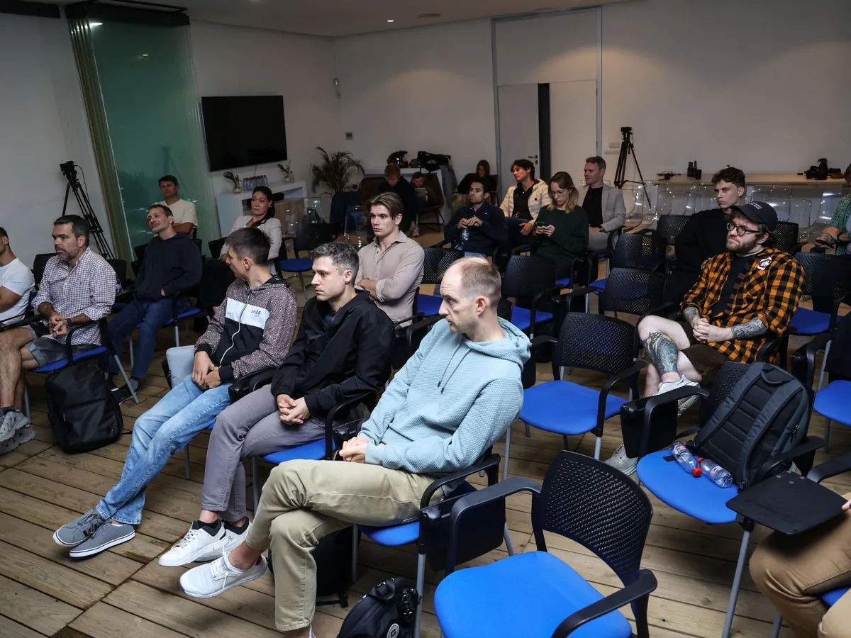 Workshop attendees on blue chairs, listening to a talk.