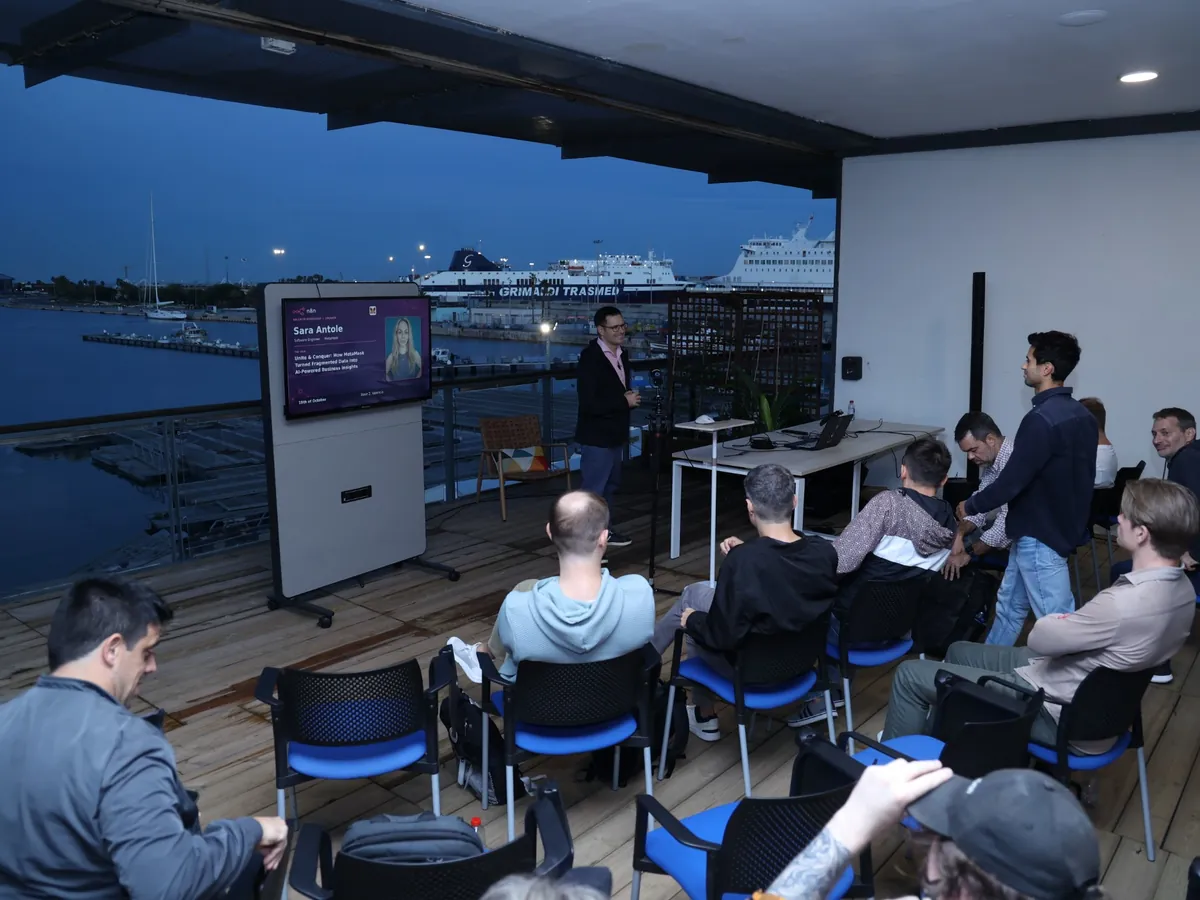 The workshop at dusk: the screen introduces Sara Antole's MetaMask talk, with the port and its lights behind.